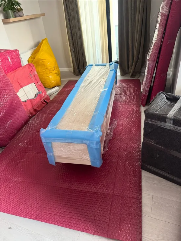Halı üzerinde köşeleri mavi koruyucuyla sarılmış ahşap sehpa