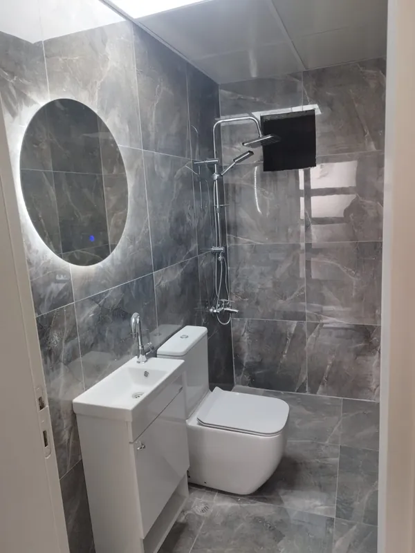 Gri fayanslı, tepe duşlu ve aydınlatmalı aynalı yenilenmiş banyo