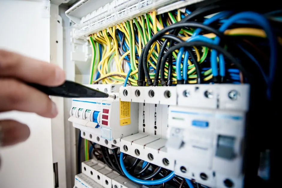 Renkli tellerle devre kesici panelinde çalışan elektrikçinin eli, elektrik bağlantılarını güvence altına alıyor.
