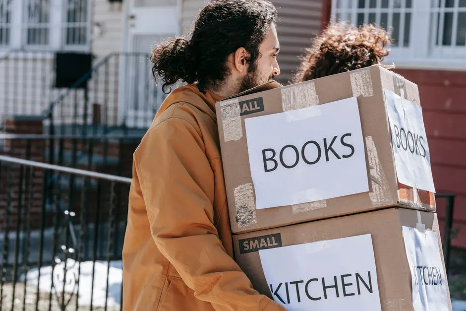 Etiketli kutuları dışarı taşıyan bir çift, yeni bir eve taşınmayı simgeliyor.