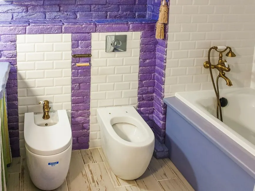 Şık bir banyo, canlı mor ve beyaz karolarla birlikte bir bidet ve küvet barındırıyor.
