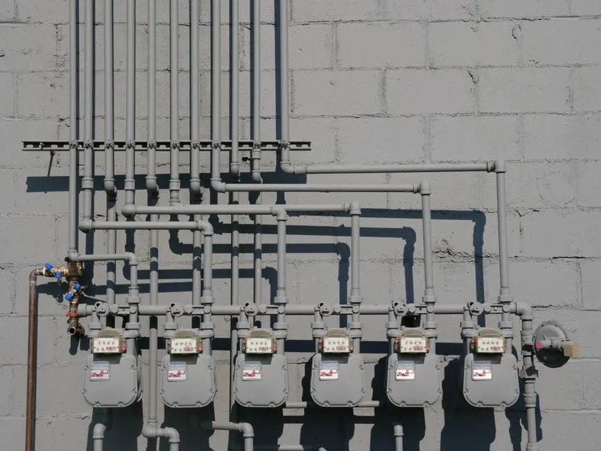 Beton bir duvara monte edilmiş doğalgaz sayaçları ve boruları, kentsel altyapıyı göstermektedir.