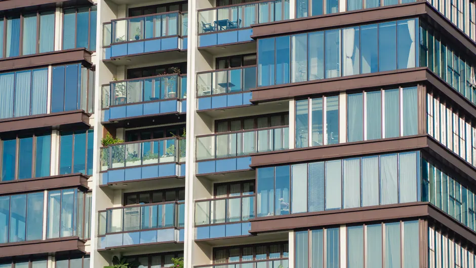 Balkonlar ve yansımalarla modern cam apartman cephesinin yakın çekim görüntüsü.