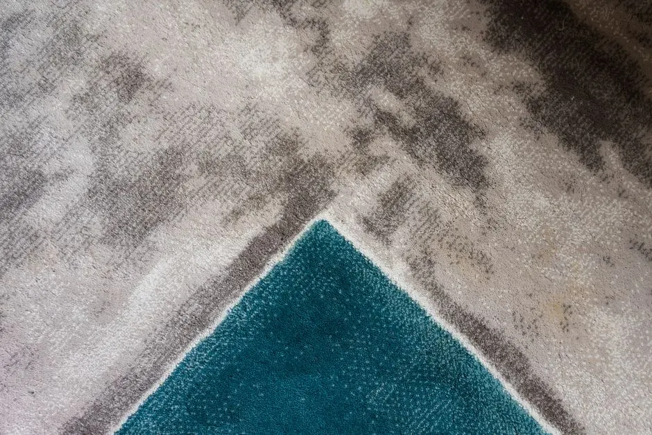 Teal ve gri tonları ile modern bir geometrik halının dokusunun yakından görüntüsü.