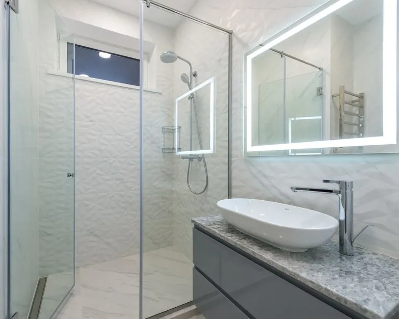 Şık, modern bir banyo; içinde yürüyüş alanı duşu ve LED aydınlatmalı ayna bulunuyor.