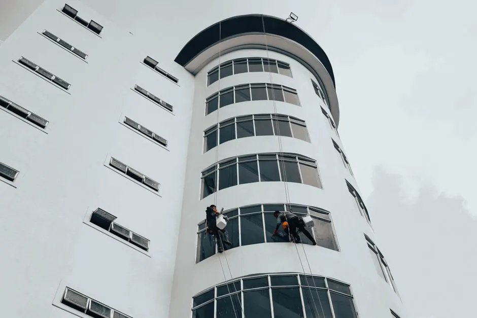 Modern bir gökdelenin camlarını iplerle temizleyen işçiler. Kentsel mimari bakım.