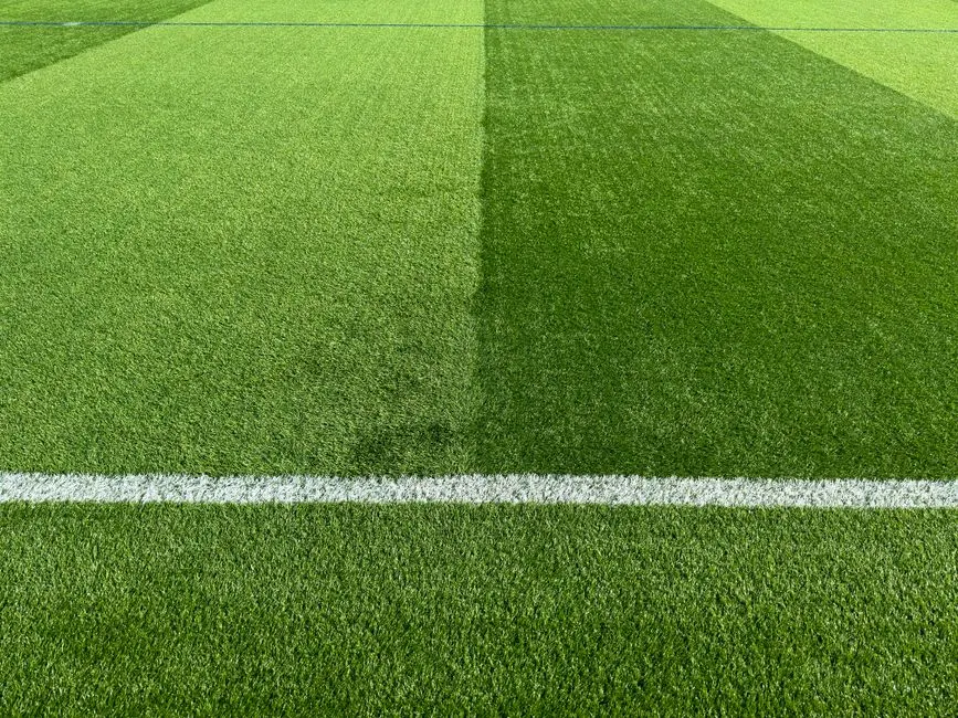 Beyaz çizgiyle işaretlenmiş canlı yeşil futbol sahasının yakın planı, spor alanının dokusunu vurguluyor.