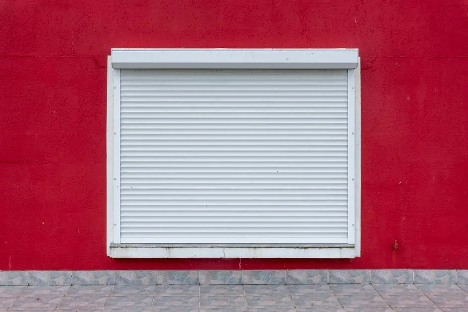 Canlı kırmızı bir duvarda yer alan beyaz bir panjurun minimalist dış görünümü.